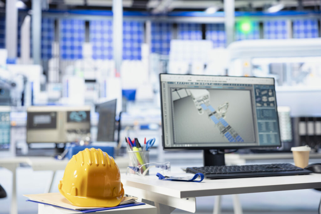 CAD program on PC display in photovoltaics factory used for designing production lines. Simulation software on computer monitor in empty solar panels plant next to yellow hardhat